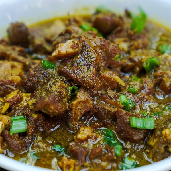 Close-up of Miss Conduck's Caribbean stew, featuring tender meat in a rich, savory sauce with green onions.
