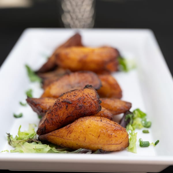 A white rectangular plate filled with golden-brown fried plantains and garnished with green lettuce.